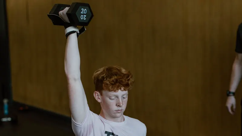 Teen athlete pressing a dumbbell overhead in the youth program at CrossFit Spring Hill